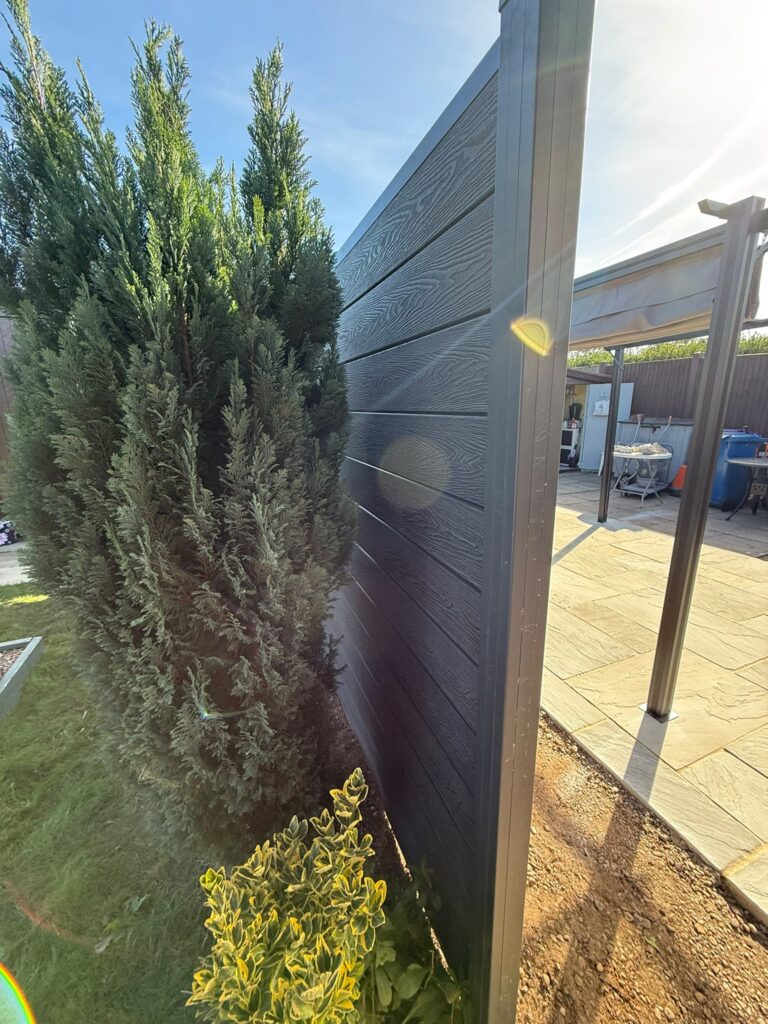 Grey woodgrain composite fence panel and aluminium post beside a conifer, fitted by fencing installers in Lincoln