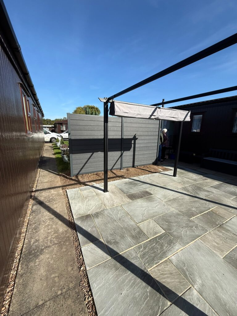 Sandstone patio, pergola and grey composite fencing along the side of a park home, installed by landscapers in Lincoln