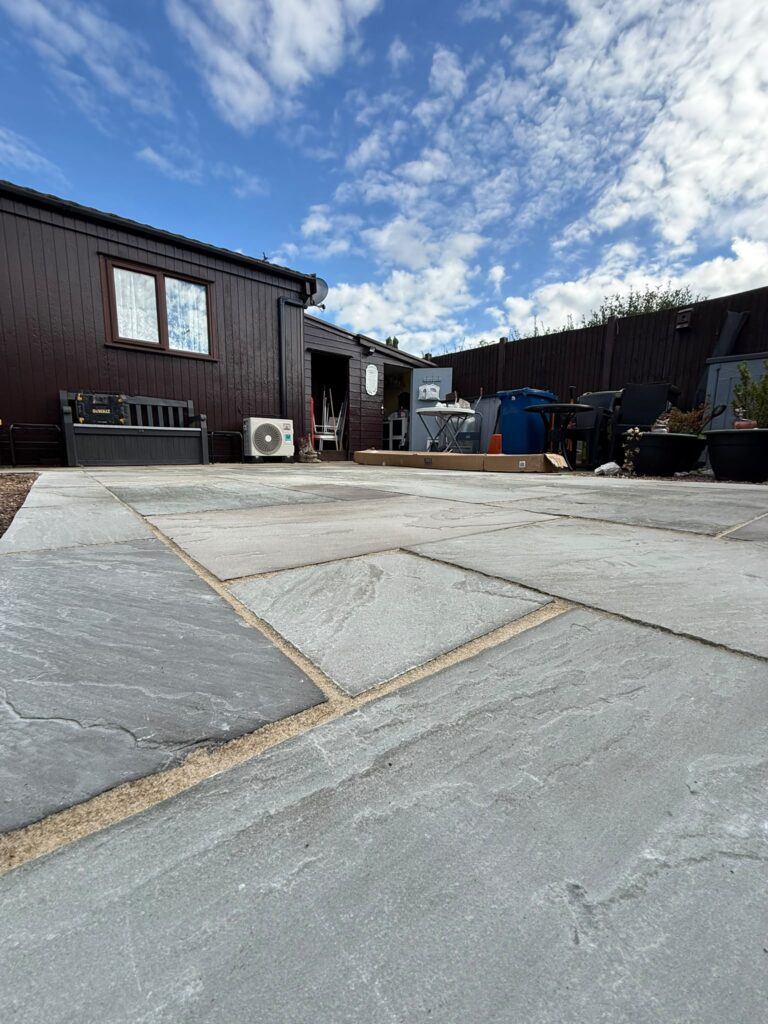 Low-level view across riven grey sandstone paving with sand-coloured pointing on a patio outside a park home