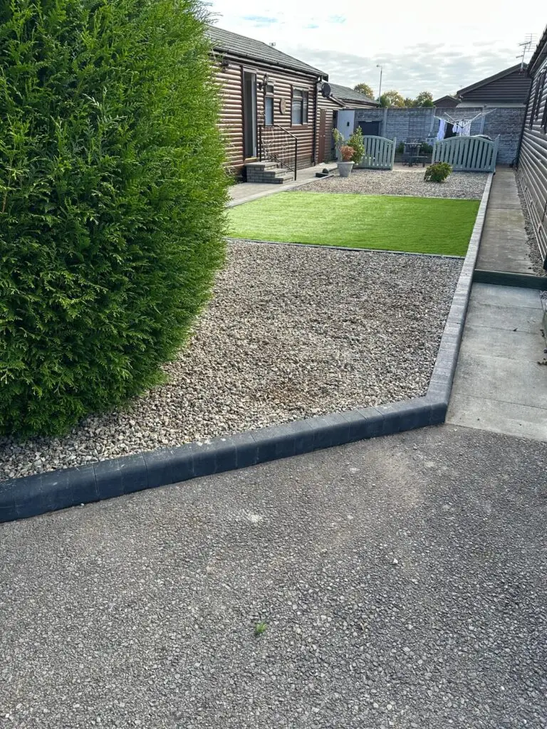 Artificial grass and gravel garden installation landscapers in Lincoln featuring clean grey kerb edging, decorative golden gravel and a green low maintenance lawn beside wooden lodge homes