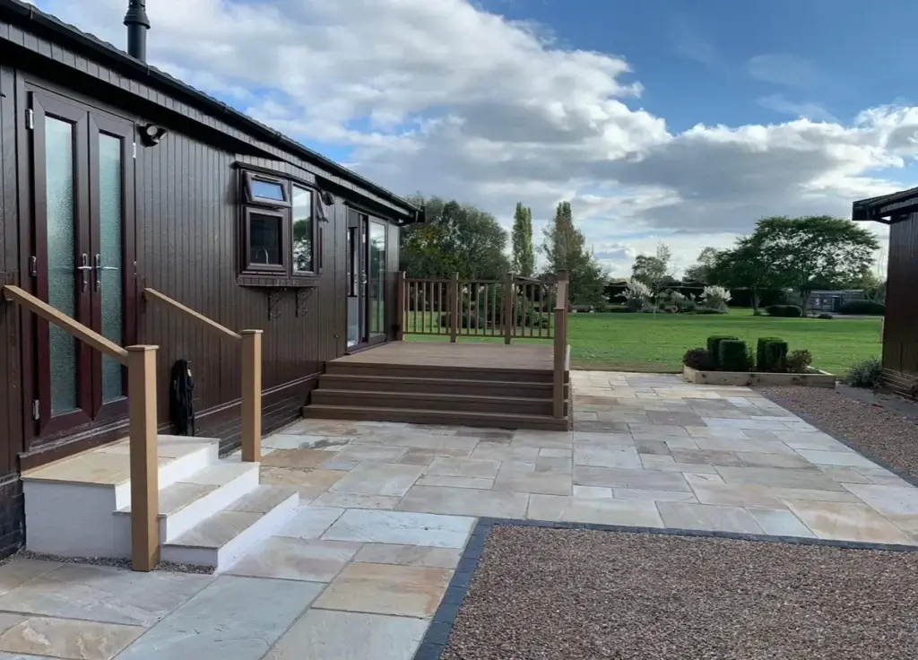 Cream sandstone patio with composite decking steps leading to a timber lodge on The Elms, Lincoln