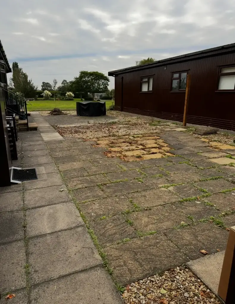 Before photo showing an old uneven concrete patio with worn paving slabs and overgrown joints at The Elms, Torksey near Lincoln. Outdoor renovation area prepared for new composite decking installation by landscape gardeners