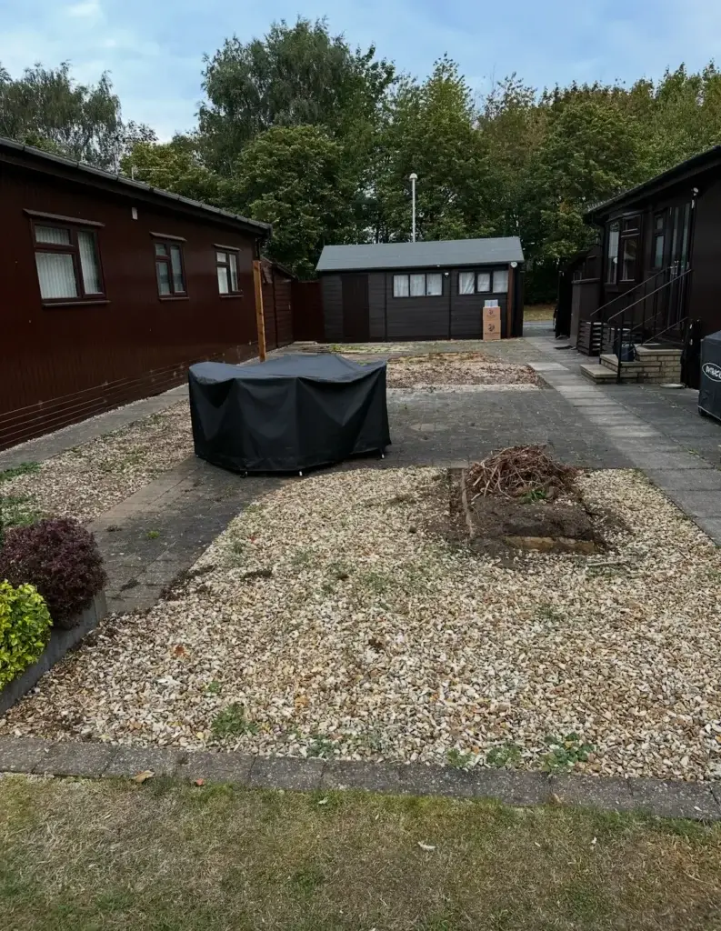 Before photo of a garden at The Elms, Torksey near Gainsborough showing a worn gravel and concrete patio with sparse planting and uneven ground, photographed prior to a full garden makeover by Reshape Landscaping in Lincoln
