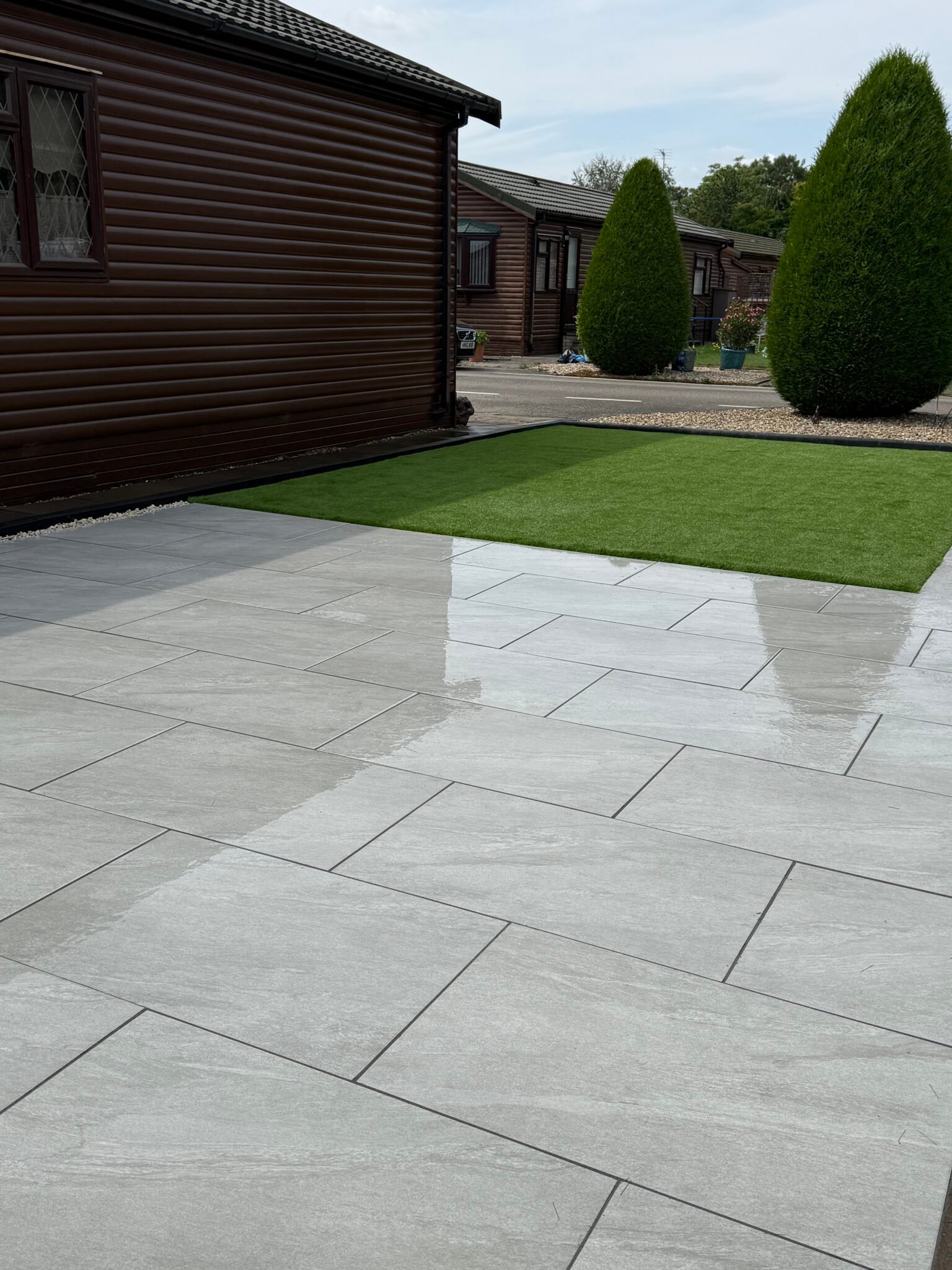 Light grey porcelain patio installation in Gainsborough The Elms by landscape gardeners featuring smooth large-format slabs and low-maintenance artificial lawn