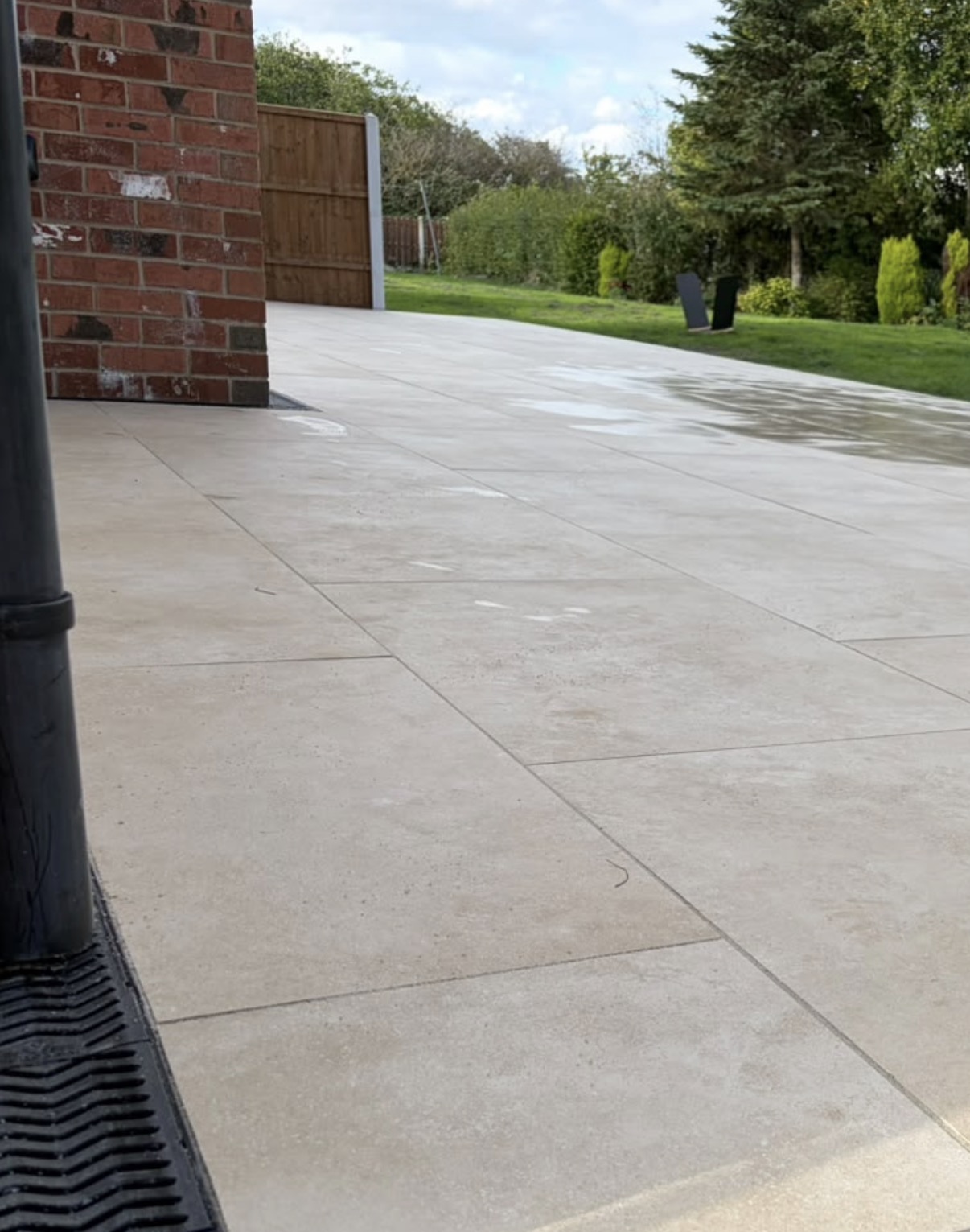 Close-up of cream patio paving with narrow joints and a drainage channel alongside the brick house.