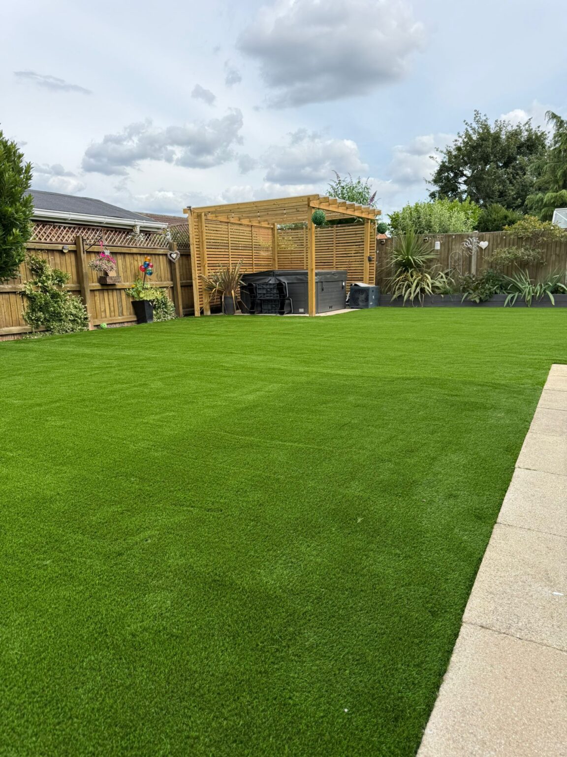 Artificial grass lawn with a timber pergola and slatted screens, installed by Reshape Landscaping in Cherry Willingham