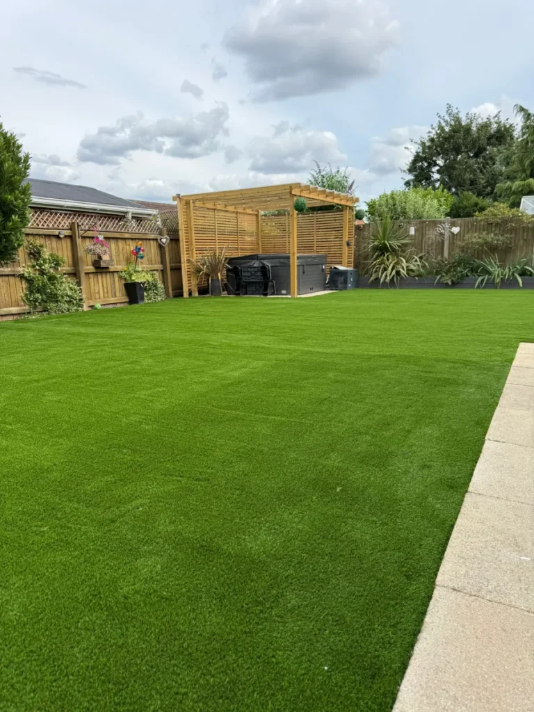 Artificial grass lawn with a timber pergola and slatted screens, installed by Reshape Landscaping in Cherry Willingham