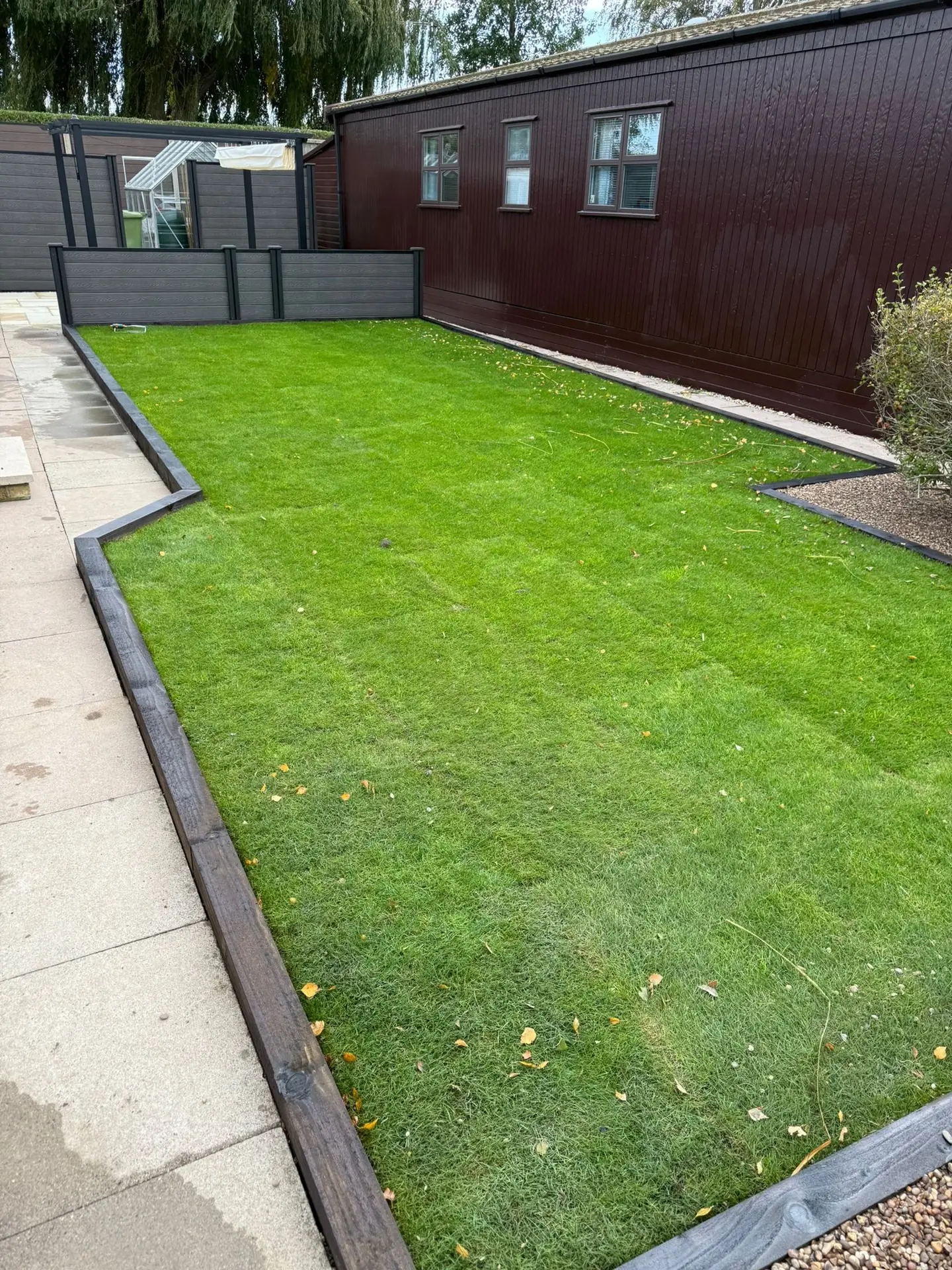 Freshly laid turf with a dark timber edge along a paved path beside a timber lodge, by landscapers in Lincoln