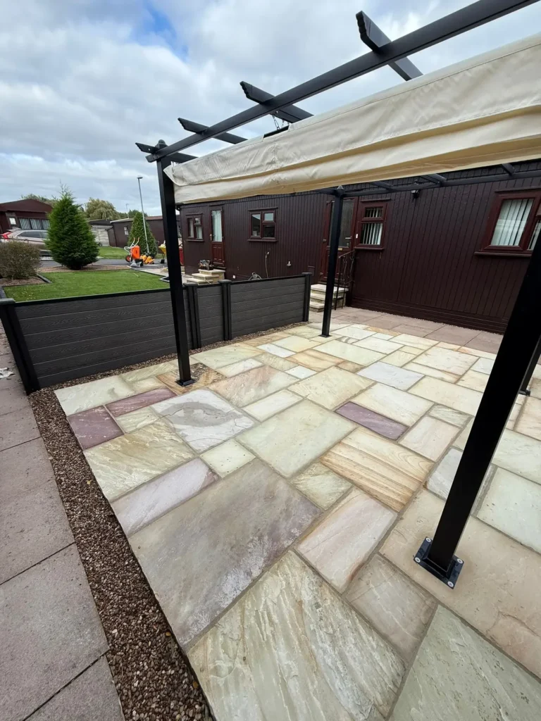 Indian sandstone patio in cream, buff, and grey tones with a modern pergola structure and composite fencing, creating a stylish outdoor entertaining area. Installed by Lincoln based landscape gardeners.