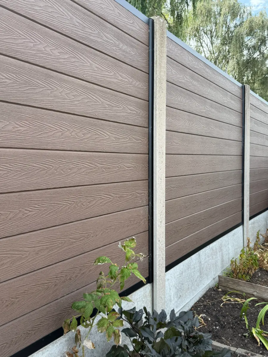 Brown woodgrain composite fence panels in concrete posts above concrete gravel boards in a Lincoln garden