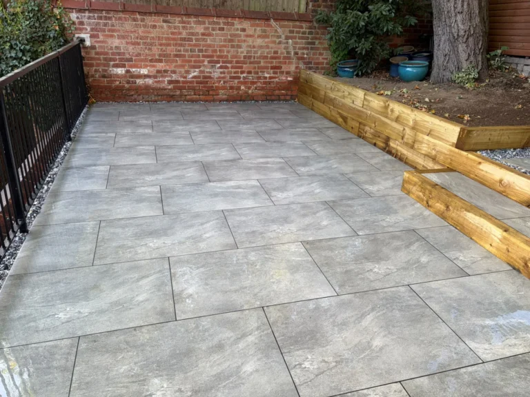 Large-format grey porcelain patio laid in a staggered pattern at an old schoolhouse in Lincoln, beside timber sleeper steps and a raised bed, by Reshape Landscaping Ltd