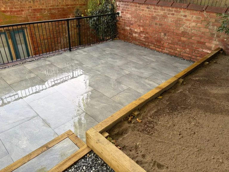 Grey porcelain patio edged in timber sleepers with a gravel border along the brick boundary wall of an old schoolhouse in Lincoln
