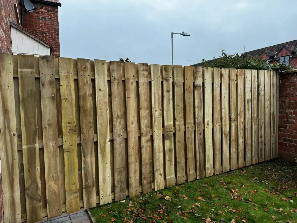 Vertical boarded timber fence enclosing the corner of a rear lawn beside a brick house wall in Lincolnshire